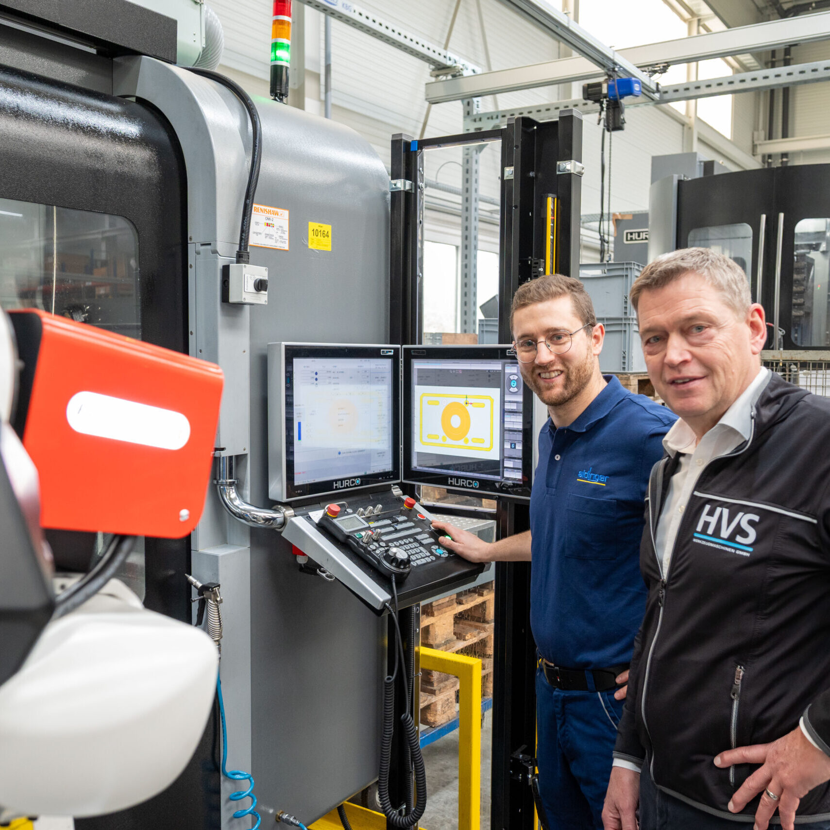Thomas Schunn und Thomas Bär vor einem HURCO-Bearbeitungszentrum mit RoboJob-Roboterautomation