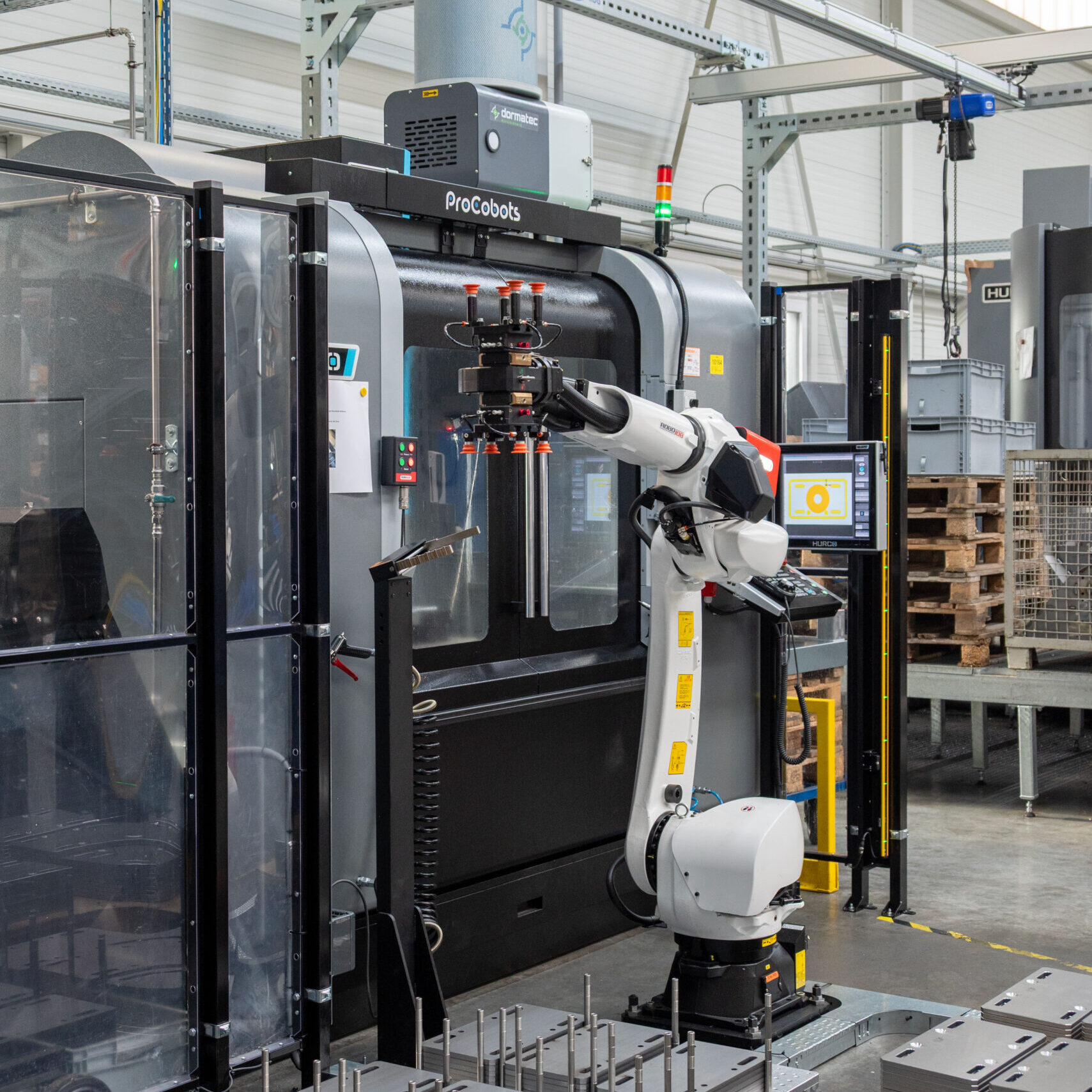 RoboJob-Roboter in Warteposition vor geschlossener HURCO-Anlage während der Bearbeitung