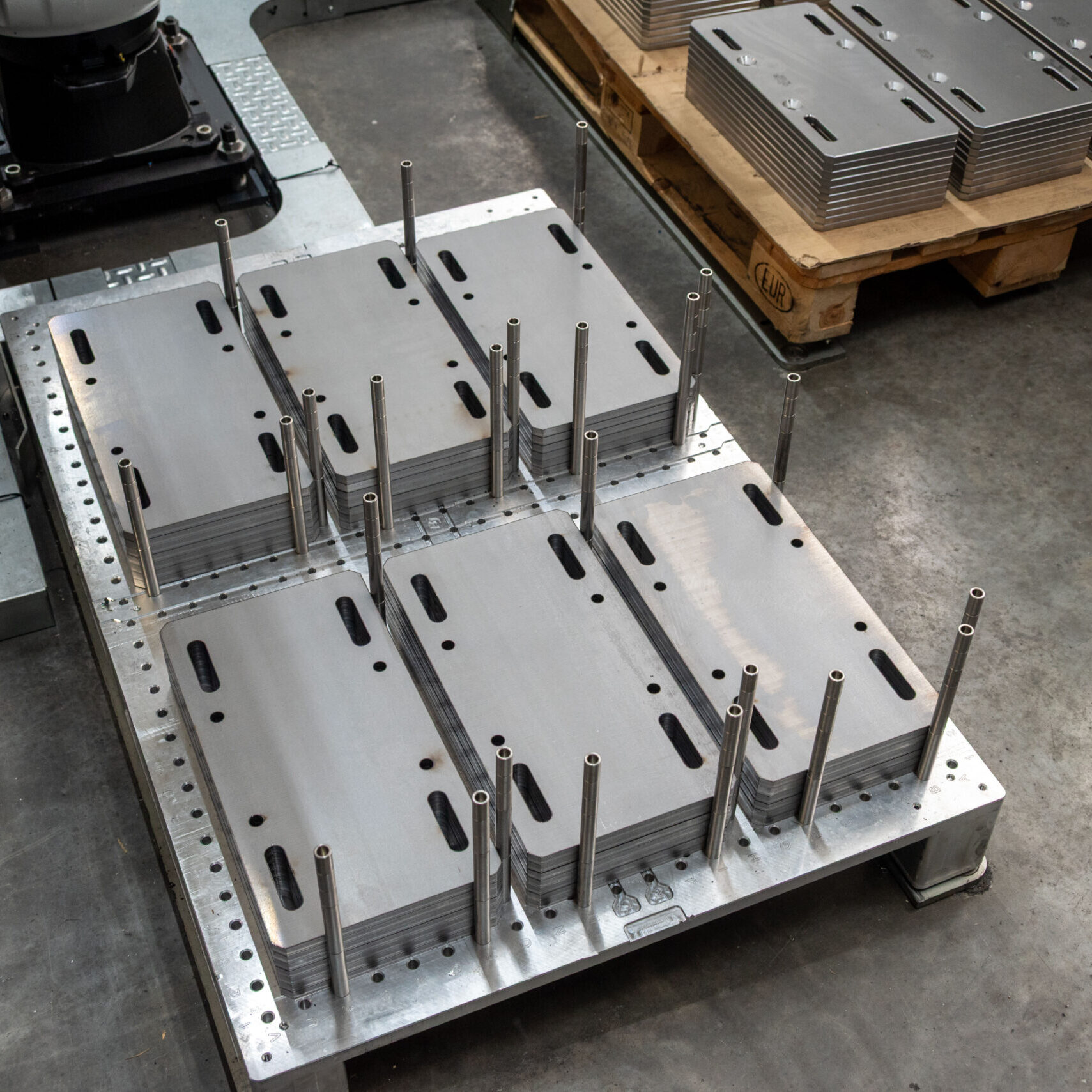 Palette mit unbearbeiteten Werkstücken und Positionierungsstäben für das Roboterhandling