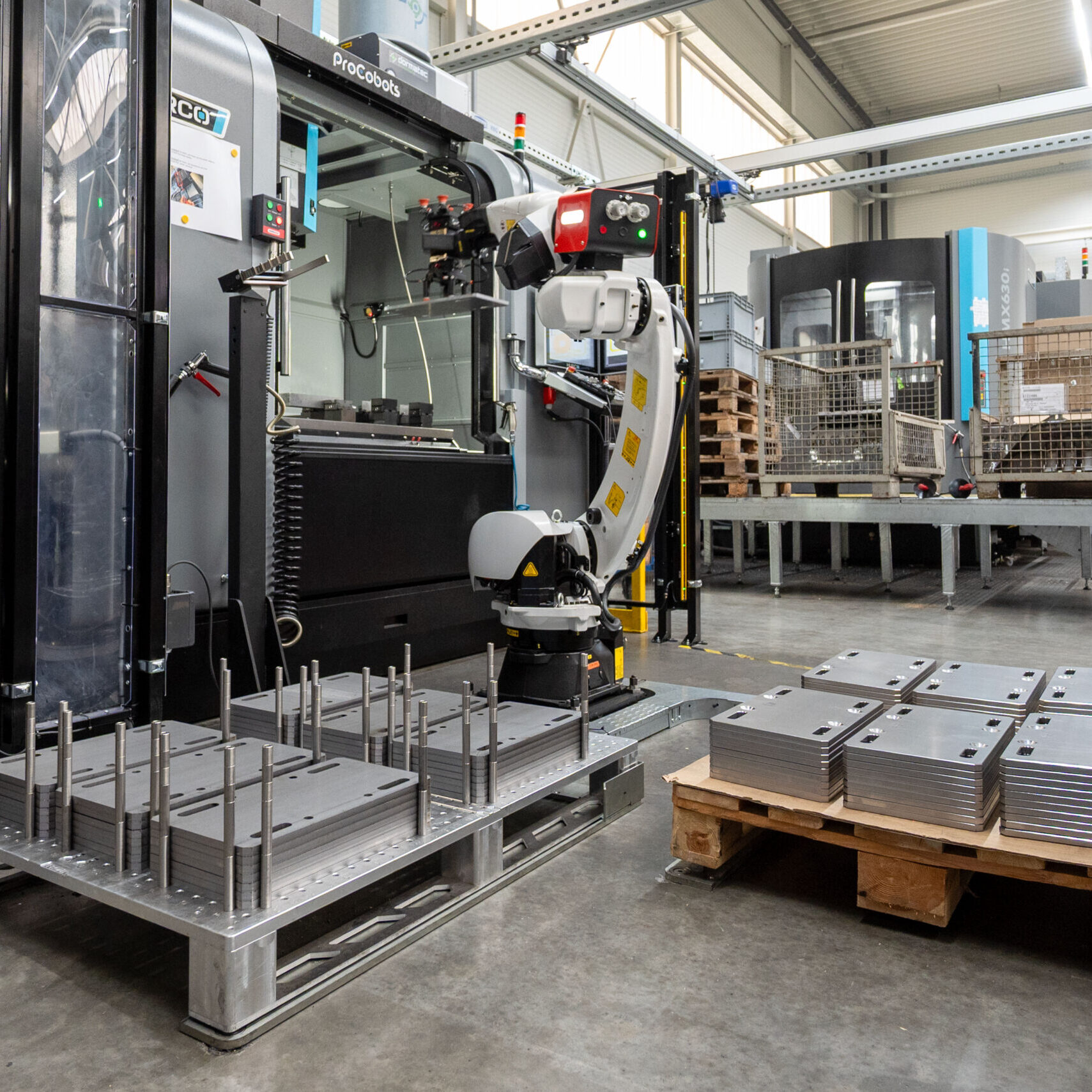 RoboJob-Roboter mit Werkstück im Prozess vor HURCO-Anlage, beide Paletten im Bild