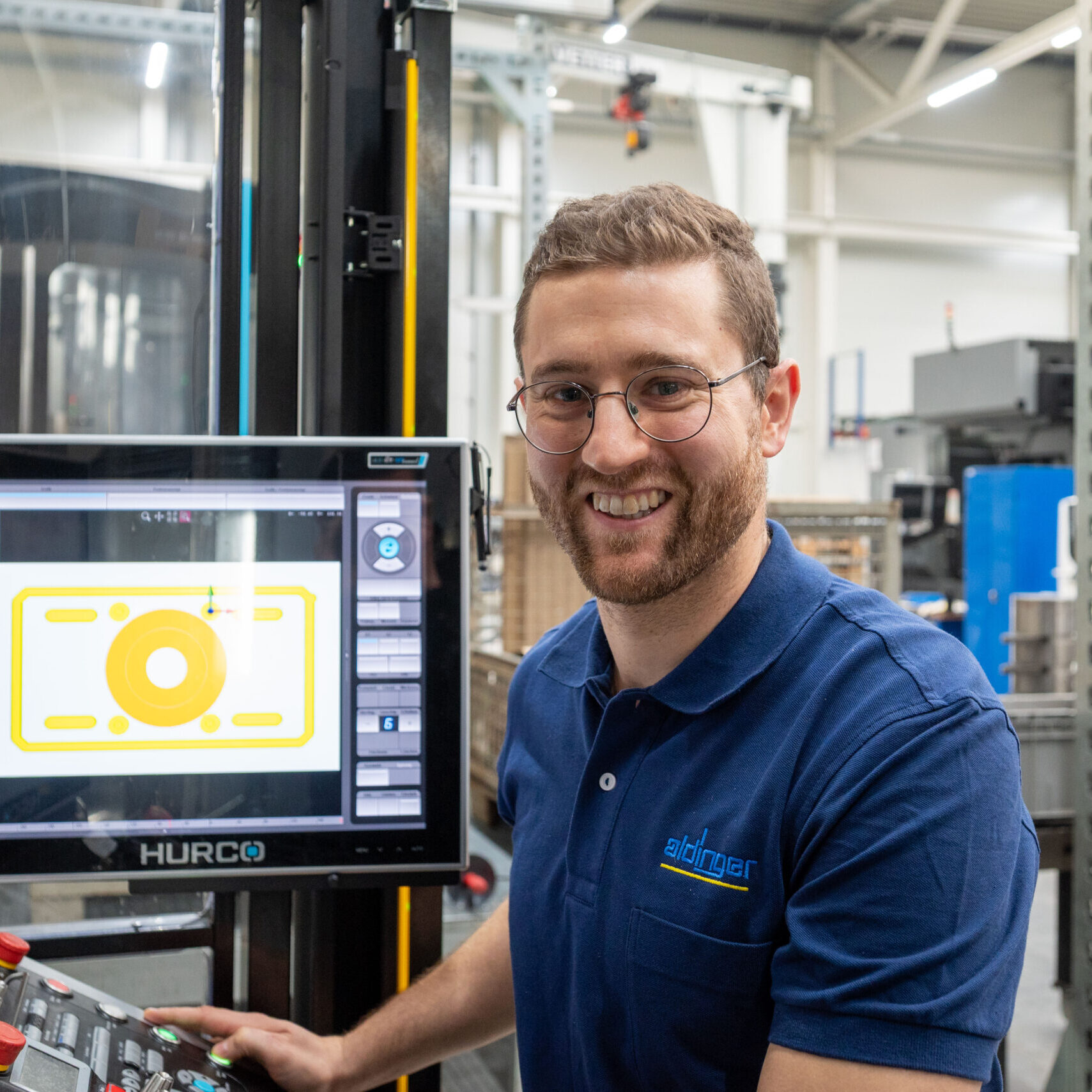 Thomas Schunn (Aldinger) an der HURCO-Maschine, lächelnd in die Kamera blickend