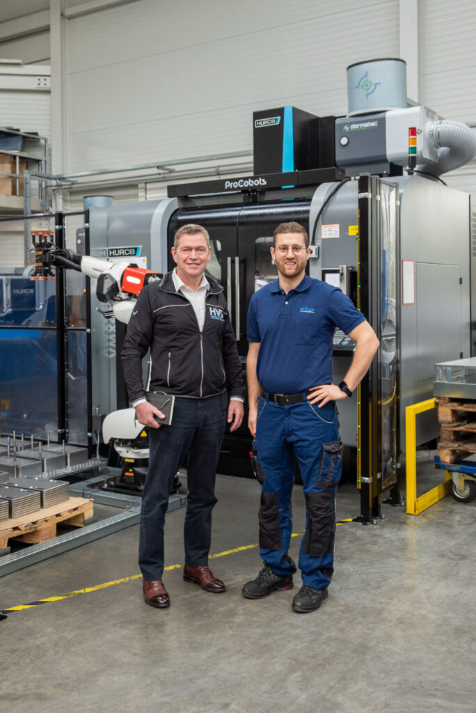 Thomas Bär (links) und Thomas Schunn an einer Roboterautomation mit 3-Achs-Bearbeitungszentrum und Wendestation